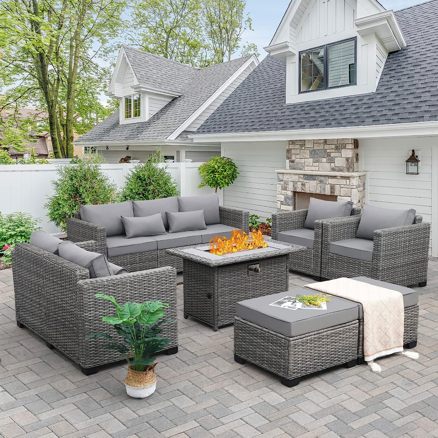 A 7-piece Rattaner fire pit patio furniture set in grey, featuring outdoor chairs, a 45-inch couch, and a wicker propane fire pit table.